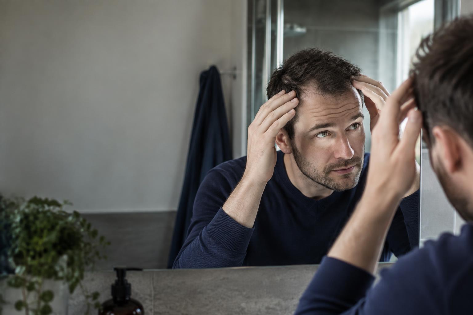 Man checking early hair transplant regrowth in a mirror